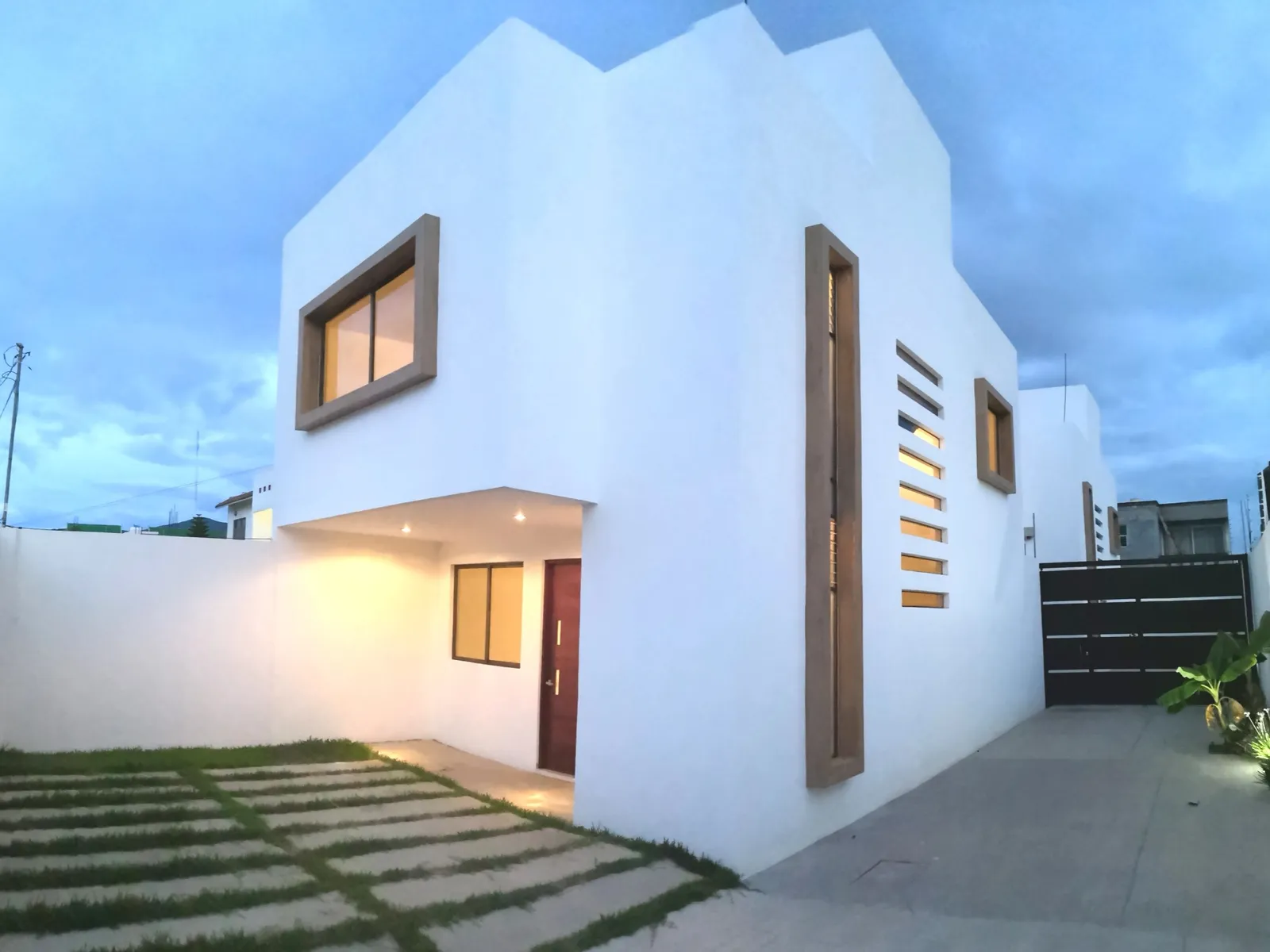 Casa de dos plantas al anochecer, con marcos de madera y celosía vertical
