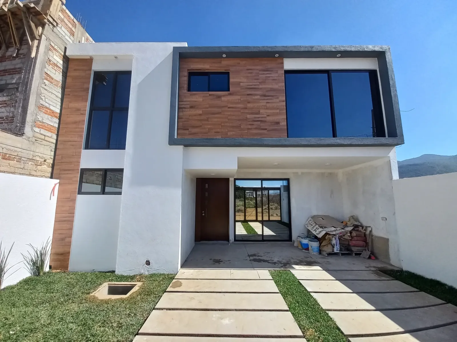 Casa de dos plantas con aplanado blanco, revestimiento de madera y cochera