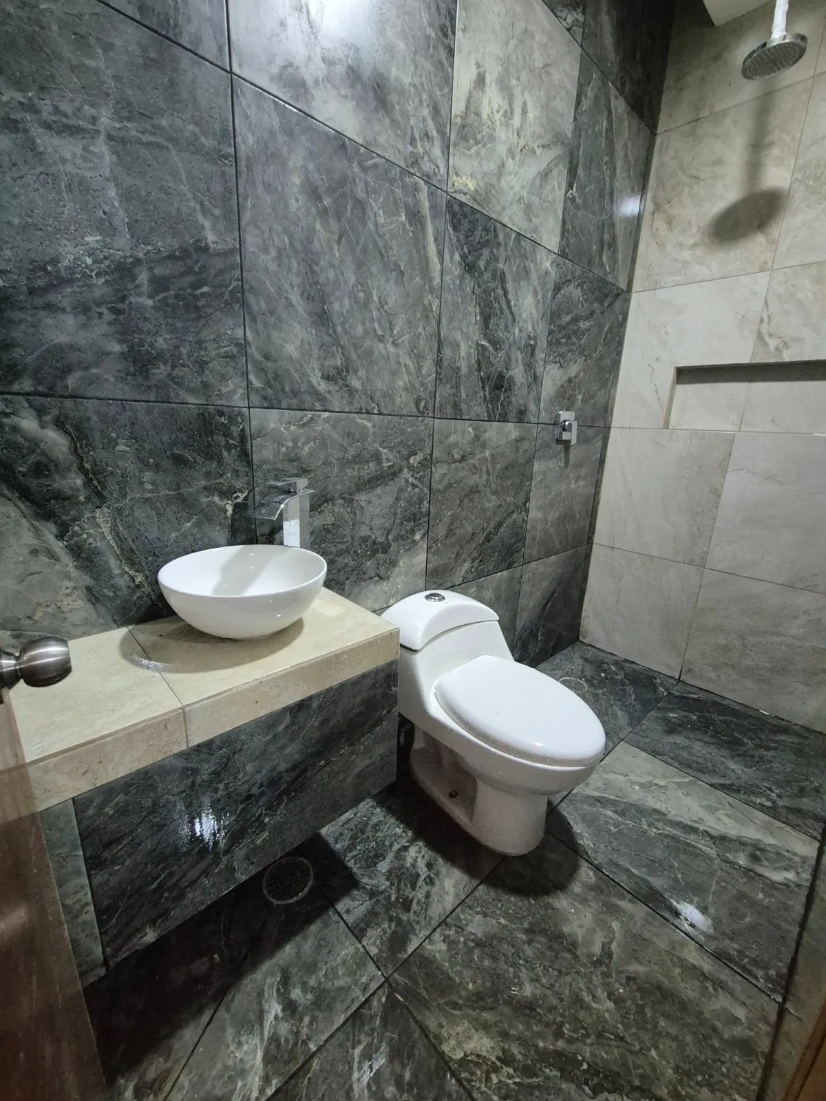 Baño terminado en mármol gris, con lavabo de sobreponer y regadera