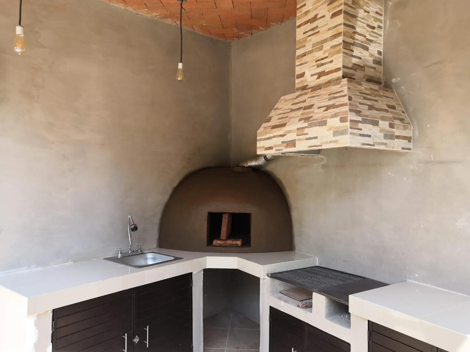 Cocina exterior con horno de leña, campana revestida en piedra y bóveda de ladrillo