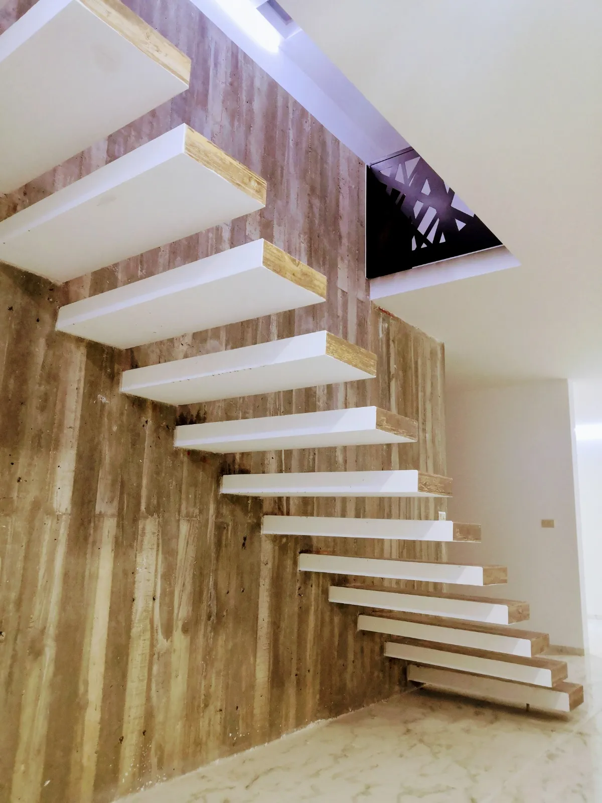 Escalera volada de peldaños blancos sobre muro de travertino