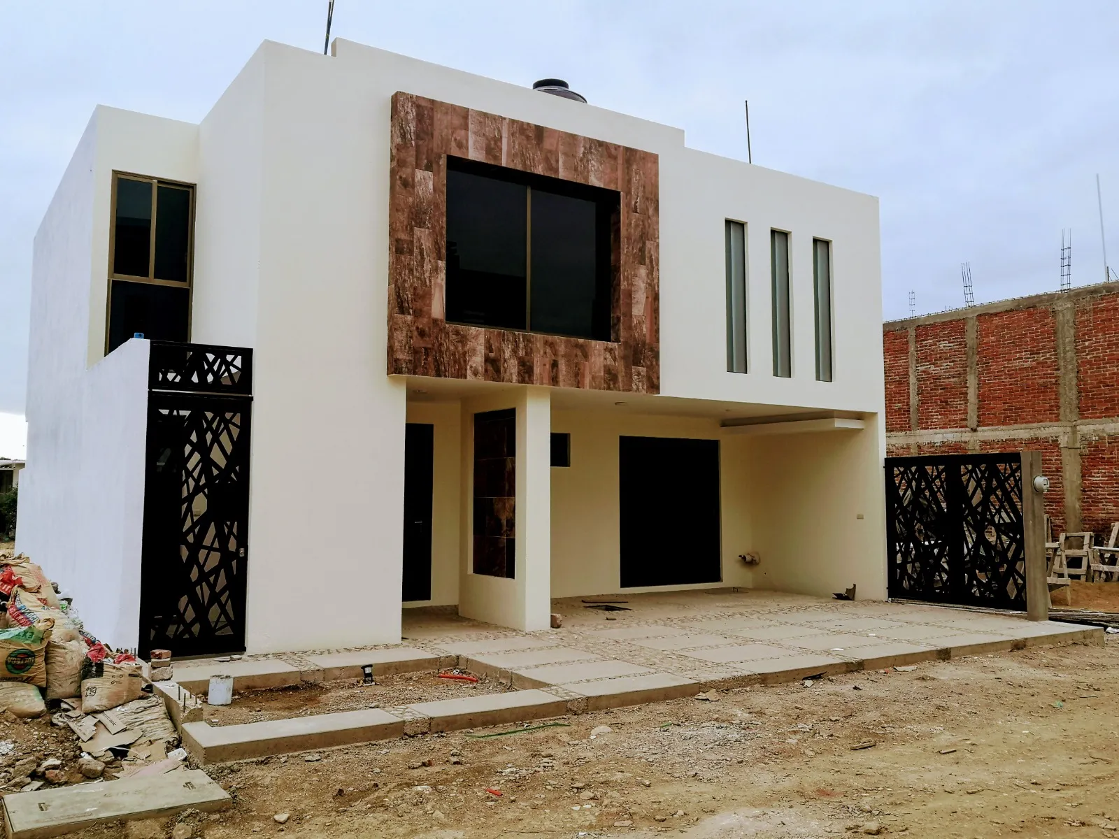 Casa de dos plantas recién terminada, con panel de piedra en el volumen superior y portones metálicos calados