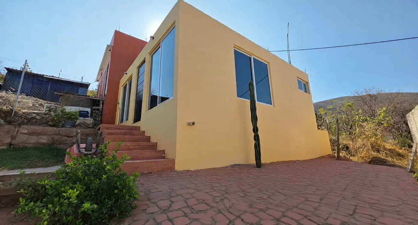 Casa de una planta con fachada amarilla y naranja, ventanal azul y andador de piedra