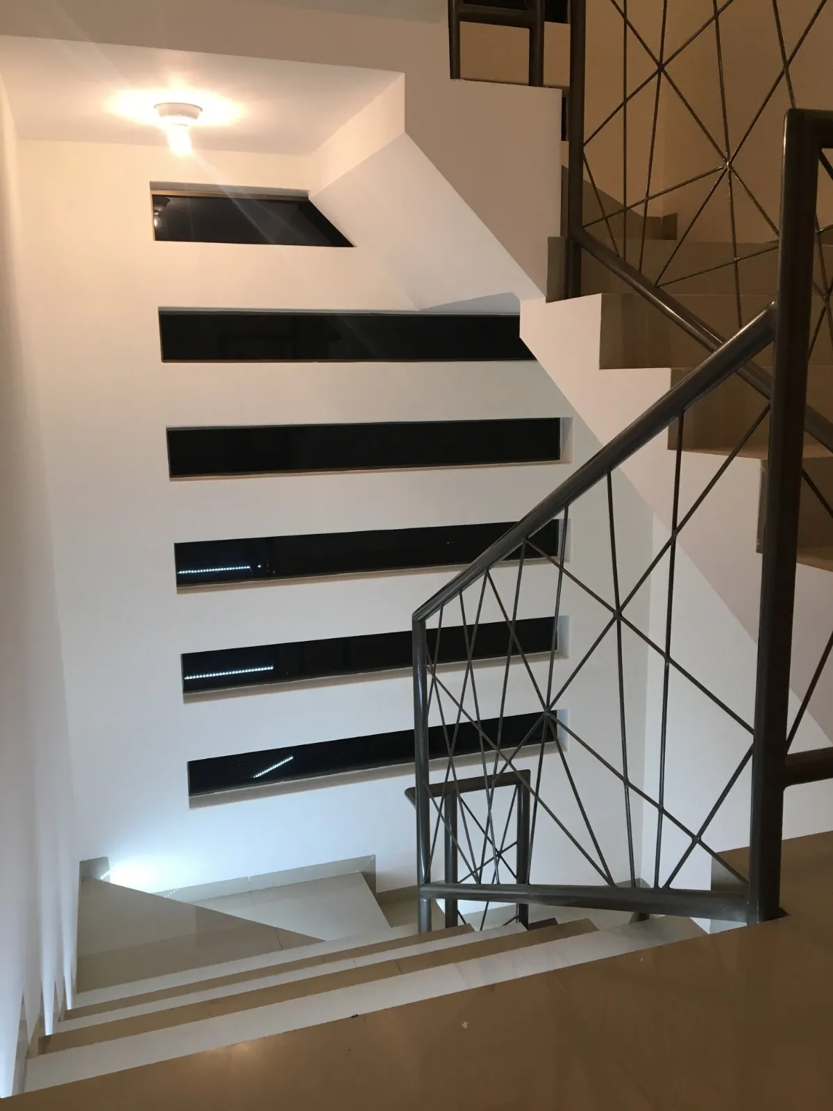 Escalera interior con nichos iluminados y barandal metálico de trama geométrica